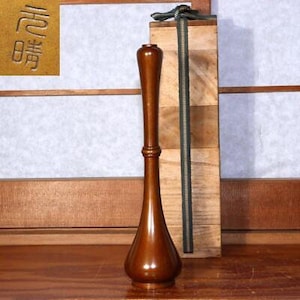 May include: A dark brown wooden vase with a rounded bottom and a narrow neck. The vase is sitting on a wooden surface.