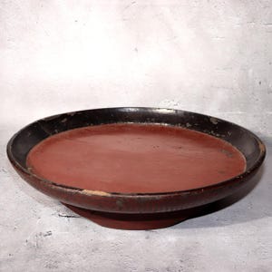 以下が含まれることがあります： 赤茶色の内側と濃い茶色の縁を持つ、丸いアンティークの木製トレイ。 トレイはロープロファイルで、わずかに隆起したベースがあります。 表面には使用感があり、ヴィンテージ感を高めています。 トレイは、サービングまたはディスプレイに使用される可能性があります。