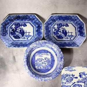 Puede incluir: Una colección de vajilla de porcelana azul y blanca. Dos platos octogonales presentan una escena central con un pájaro y una valla, rodeada de motivos florales. Un cuenco redondo y un plato cuadrado pequeño con diseños similares completan el conjunto.