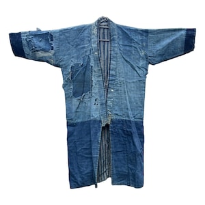 May include: A long-sleeved indigo-dyed boro kimono featuring multiple shades of blue, visible patches, and frayed fabric sections. The garment displays a layered construction with a dark blue lower panel and a striped inner lining visible at the front.