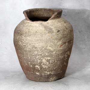 Puede incluir: Un jarrón de cerámica de estilo antiguo y desgastado, con una abertura amplia e irregular. El jarrón tiene un cuerpo redondeado y una superficie texturizada con una mezcla de tonos marrones, beige y rojizos. La apariencia envejecida sugiere que es una pieza decorativa antigua.