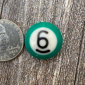 May include: A green and white billiard ball with the number 6 printed on it.