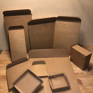 Może przedstawiać: Zbi&oacute;r brązowych kartonowych pudełek o r&oacute;żnych rozmiarach i kształtach. Niekt&oacute;re pudełka mają klapę na g&oacute;rze, podczas gdy inne mają przezroczyste plastikowe okienko. Pudełka są idealne do pakowania i wysyłki małych przedmiot&oacute;w.