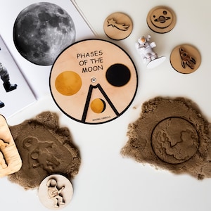Peut inclure: Jouet en bois représentant les phases de la lune. Le jouet est un disque circulaire avec une image en noir et blanc de la lune au centre. Le disque est divisé en huit sections, chacune montrant une phase différente de la lune. Le jouet comprend également une petite figurine d'astronaute en bois et une fusée en bois.