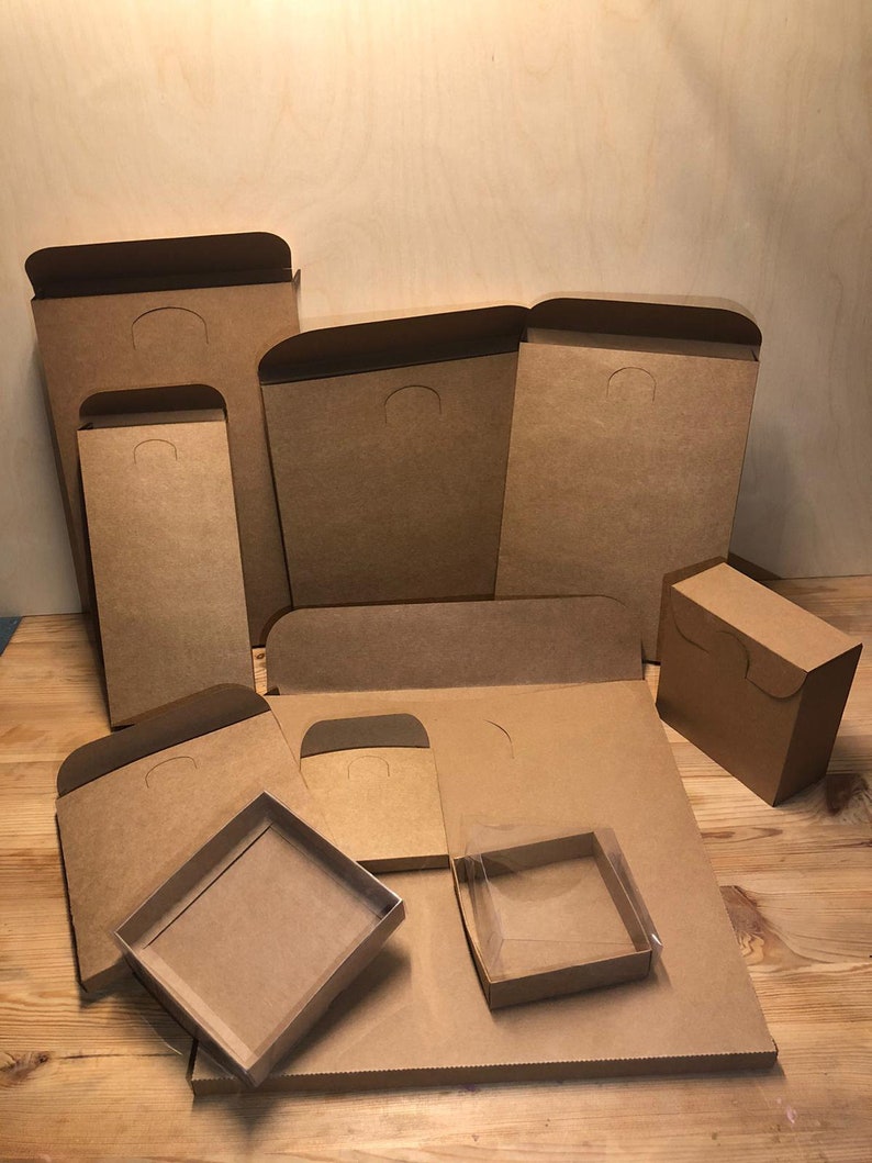 May include: A collection of brown cardboard boxes of various sizes and shapes. Some boxes have a flap with a cut-out handle. One box has a clear plastic window.