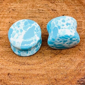 May include: A pair of blue and white marbled ear gauges. The gauges are shaped like a cylinder with a slight flare at the top and bottom.