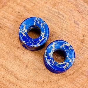 May include: Two blue and gold marbled stone ear gauges. The gauges are round with a hole in the centre.