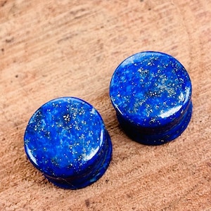 May include: Two round blue lapis lazuli stone ear gauges. The stone has a speckled pattern of gold flecks.