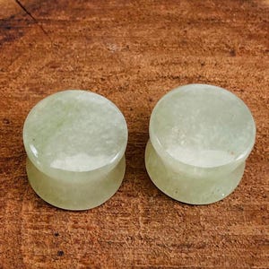 Puede incluir: Par de dilatadores de oreja de piedra verde claro. Los dilatadores son redondos y tienen un acabado liso y pulido.