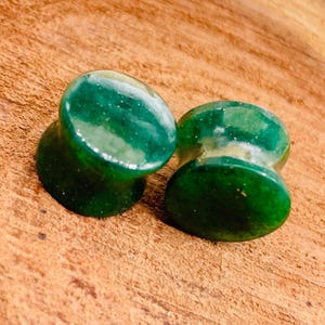 Puede incluir: Un par de dilatadores de oreja de piedra preciosa verde. Los dilatadores son redondos y tienen un aspecto moteado.