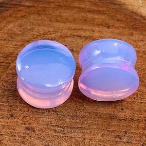 Könnte beinhalten: Paar irisierende Opal-Ohrmanschetten, eine ist ein Single Flare und die andere ein Double Flare. Die Manschetten sind hellblau mit einem rosa Farbton.