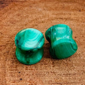 Puede incluir: Dos medidores de oreja de piedra de malaquita verde. Los medidores son redondos y tienen un patrón de remolino.