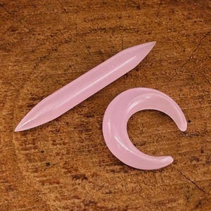 以下が含まれることがあります： 体のジュエリー用のピンク色のガラスの部品が2つ。1つは長く、細く、尖った部品で、もう1つは三日月の形です。