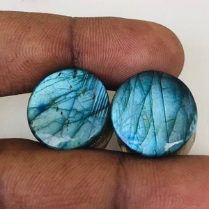 Puede incluir: Dos cabujones redondos de labradorita azul con brillo iridiscente. Los cabujones tienen un diámetro de aproximadamente 2,5 cm.