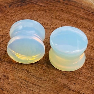 Könnte beinhalten: Zwei schimmernde Opal-Ohrenstopfen, einer ist hellblau und der andere ist ein hellerer Blauton mit einem gelben Farbton.