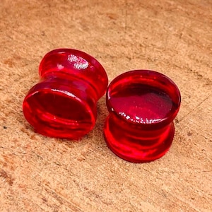 May include: Two red acrylic ear gauges, one on top of the other. The gauges are smooth and shiny.