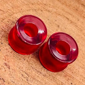 Könnte beinhalten: Zwei rote Acryl-Ohrenstrecker, einer auf dem anderen. Die Strecker sind rund und haben eine glatte, glänzende Oberfläche.