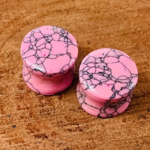 May include: Pair of pink and black marbled ear gauges. The gauges have a swirling pattern of black veins on a pink background.