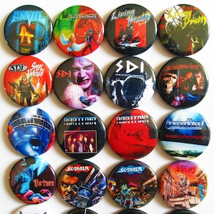 Op de afbeelding: Een verzameling van 16 ronde metalen pinback-knoppen met verschillende heavy metal bandlogo's en albumhoezen. De knoppen zijn zwart, rood, blauw, groen en wit met afbeeldingen van muzikanten, schedels en andere grafische ontwerpen. De bandnamen omvatten Anvil, Iron Angel, Living Death, Exorcist, Abattoir, Scanner, Torture, Messiah Force, Tyrant, Sarcasm en Powerlord.