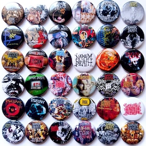 Puede incluir: Una colección de 25 botones redondos de metal con cierre de seguridad que muestran diferentes portadas de álbumes de la banda Napalm Death. Los botones están dispuestos en una cuadrícula y presentan una variedad de colores y diseños.