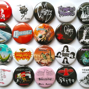 May include: A collection of 16 round button badges featuring various band logos and album artwork. The badges are black, white, red, green, and blue. The bands featured include Quartz, Praying Mantis, Trespass, Brightlights, White Spirit, and Triarche.