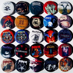 Könnte beinhalten: Eine Sammlung von 18 runden Metallpins mit verschiedenen Heavy-Metal-Bandlogos. Die Pins sind schwarz, rot, blau und weiß mit Bildern von Totenköpfen, Dämonen und anderen dunklen Bildern. Die abgebildeten Bands sind Candlemass, Pentagram, Solitude Aeturnus und Saint Vitus.