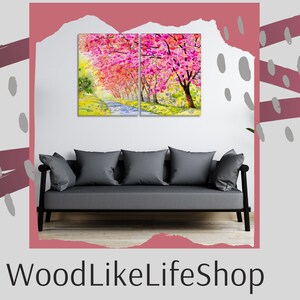 May include: A split canvas print of a watercolor painting depicting a path lined with pink cherry blossom trees. The print is hanging on a white wall above a gray sofa.