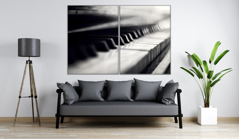 May include: A black and white photograph of a piano keyboard, split into two sections. The image is displayed in a living room setting with a gray sofa, a floor lamp, and a potted plant.