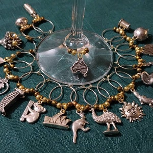 Puede incluir: Un conjunto de 14 charms para copas de vino en plata y oro que representan iconos australianos, incluyendo un koala, un canguro, un sol, un emú y la Ópera de Sídney. Los charms están unidos a una cadena de cuentas doradas.