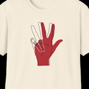 May include: Cream-colored t-shirt featuring a red and white hand gesture graphic. The design shows a red hand with a white outline, forming a unique symbol. The shirt is made of a soft material.