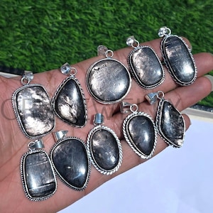 Pode incluir: Uma coleção de nove pingentes de prata com pedras de obsidiana preta. As pedras têm um efeito brilhante e iridescente. Os pingentes são de diferentes formas e tamanhos.