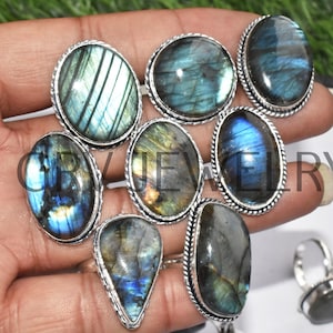 May include: A collection of eight silver rings with oval and teardrop shaped labradorite gemstones. The stones have a blue, green, and gold iridescent sheen.
