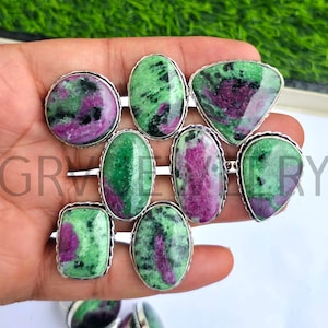 May include: A selection of gemstone rings with ruby zoisite stones. The rings have silver settings and come in various shapes, such as oval, round, and triangular. The stones exhibit a combination of green and pink colours.