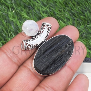 May include: A silver ring with a black oval shaped stone and a round white moonstone. The ring has a decorative design.