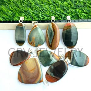 Può includere: Assortimento di otto ciondoli in pietra preziosa con montature in argento. I ciondoli sono di forma ovale e a goccia e presentano una varietà di colori, tra cui verde, marrone e nero.