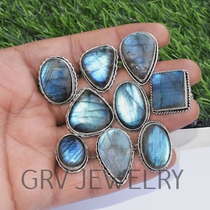 May include: A collection of ten silver rings with blue labradorite gemstones. The rings are displayed on a hand, with the gemstones facing the camera. The gemstones are all different shapes and sizes, and they have a beautiful iridescent sheen.