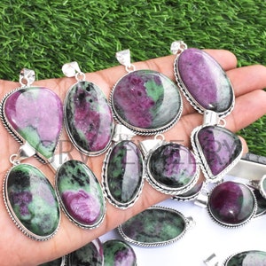 May include: A collection of green and pink gemstone pendants with silver settings. The pendants are oval, teardrop, and triangular shaped.