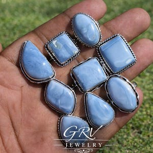 Può includere: Una collezione di anelli in argento con pietre preziose azzurre di forma ovale, quadrata e a goccia. Gli anelli sono esposti su una mano contro uno sfondo verde sfocato. Gli anelli sono di GRV Jewelry.
