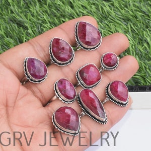 May include: Nine silver rings with red gemstone settings. The rings are displayed on a hand, with the gemstones facing the camera. The gemstones are various shapes, including oval, round, and pear.