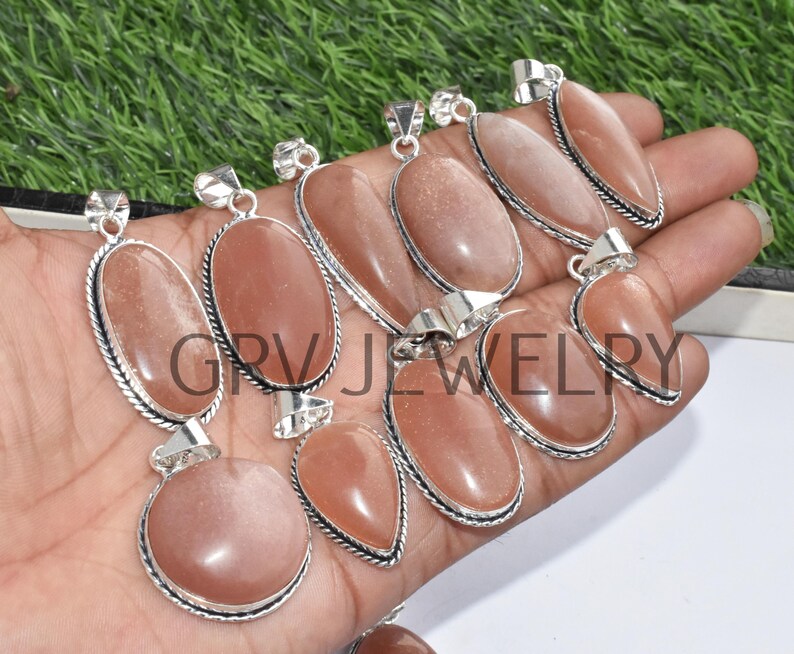 Puede incluir: Una colecci&oacute;n de 10 colgantes de piedra de sol con engastes de plata. Los colgantes son de forma ovalada y de l&aacute;grima y tienen un color naranja claro.