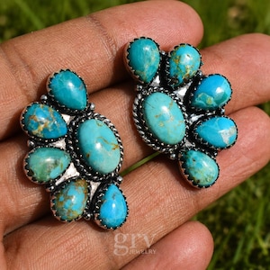 May include: A pair of silver earrings featuring multiple teardrop-shaped turquoise stones with brown matrix patterns. Each earring has a central oval stone surrounded by smaller stones in a fan-like arrangement with twisted silver wire detailing.