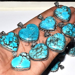 May include: A collection of turquoise heart-shaped pendants with silver settings. The pendants are arranged on a hand, showcasing their intricate details and vibrant blue colour.