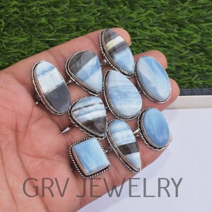 May include: A collection of nine silver rings with blue opal gemstones. The rings are arranged in a hand, with the gemstones facing up. The gemstones are all different shapes and sizes, and some have a white or black pattern.