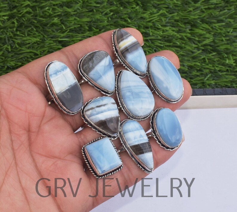 May include: A collection of nine silver rings with blue opal gemstones. The rings are arranged in a hand, with the gemstones facing up. The gemstones are all different shapes and sizes, and some have a white or black pattern.