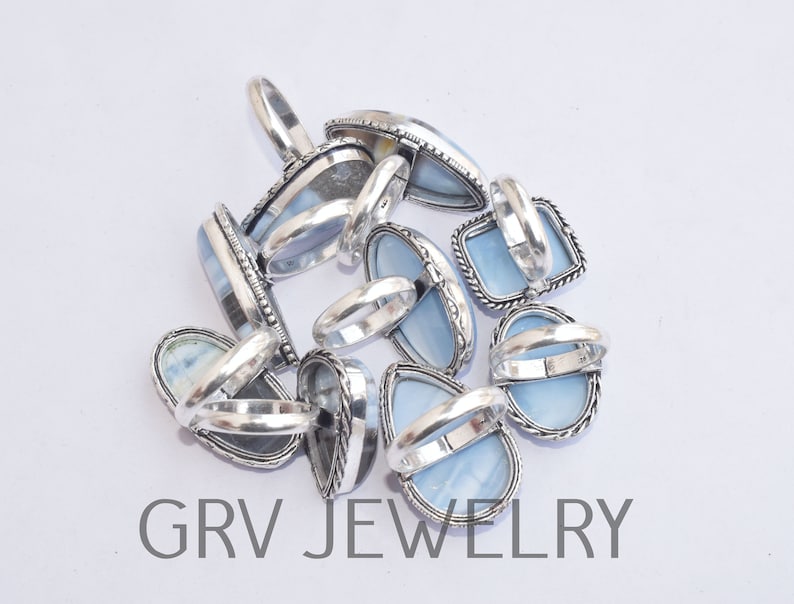 May include: A group of silver rings with blue opal stones. The rings are stacked on top of each other and the stones are facing up. The rings are all different shapes and sizes.