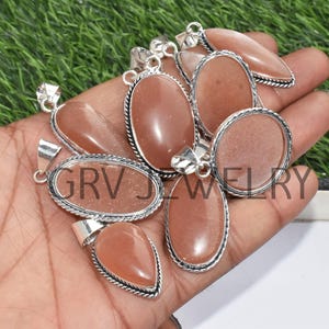 Puede incluir: Un grupo de ocho colgantes de plata con piedras preciosas de piedra de sol de color melocot&oacute;n. Los colgantes son de forma ovalada y en forma de l&aacute;grima y tienen un engaste de plata.