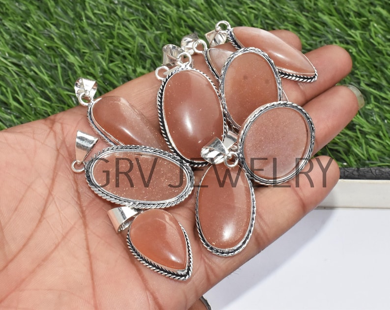 Puede incluir: Un grupo de ocho colgantes de plata con piedras preciosas de piedra de sol de color melocot&oacute;n. Los colgantes son de forma ovalada y en forma de l&aacute;grima y tienen un engaste de plata.