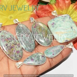 Puede incluir: Cinco colgantes de plata con piedras preciosas de zoisita rubí verde y rosa. Los colgantes son de forma ovalada, de lágrima y rectangular. Los colgantes están en una mano.