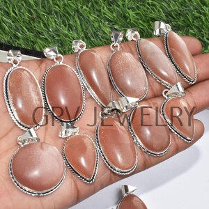 Puede incluir: Una colecci&oacute;n de diez colgantes de piedra de sol con engastes de plata. Los colgantes son de forma ovalada y de l&aacute;grima y tienen un color naranja claro.
