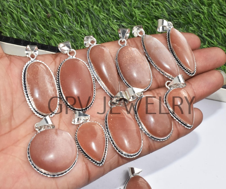 Puede incluir: Una colecci&oacute;n de diez colgantes de piedra de sol con engastes de plata. Los colgantes son de forma ovalada y de l&aacute;grima y tienen un color naranja claro.
